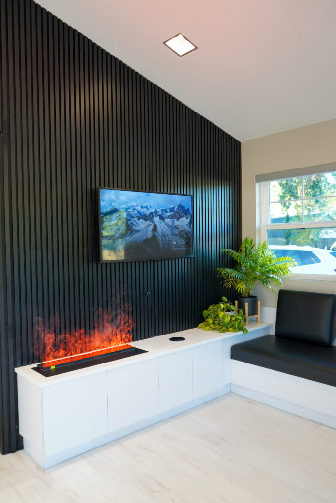 A luxury dental waiting room at Mona Lisa Smile Dental featuring a modern fireplace flat screen television and comfortable black leather seating.